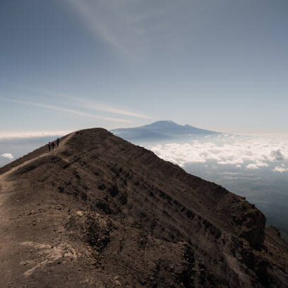 Hikers walking along the crater rim of mount meru, tanzania, africa, with kilimanjaro in the background